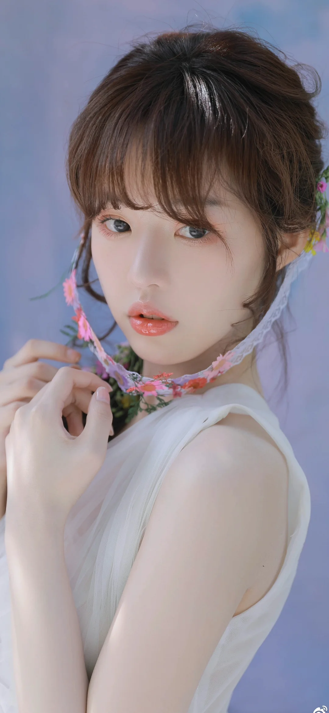 一位成年女性佩戴花环项链，在浅紫色背景前注视镜头。