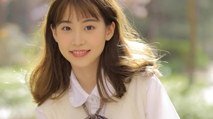 一名长发女性在户外阳光下微笑，背景呈现柔和的绿色虚化光影。