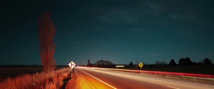 夜色中的乡间公路延伸向远方，车灯形成明亮的光轨，背景是星空与田野。