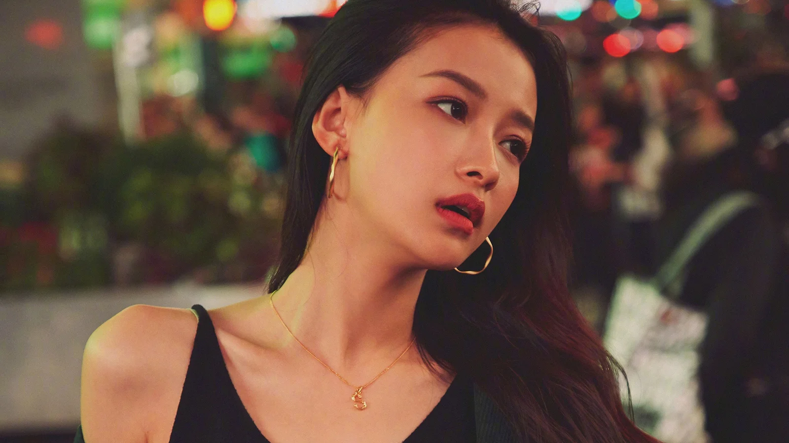 一名成年女性在背景灯光虚化的室内环境中侧头注视镜头外。