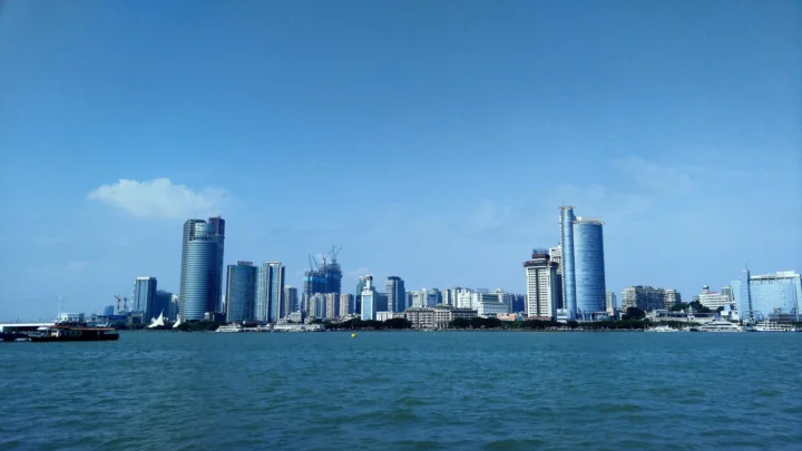 蓝天下，海面前方是一座由高层建筑组成的现代城市天际线。