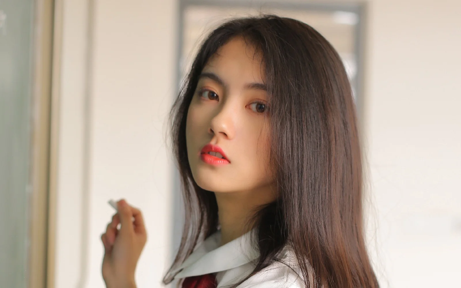 긴 머리의 여성이 흰색 칼라 상의를 입고 실내에서 카메라를 바라보고 있습니다.
