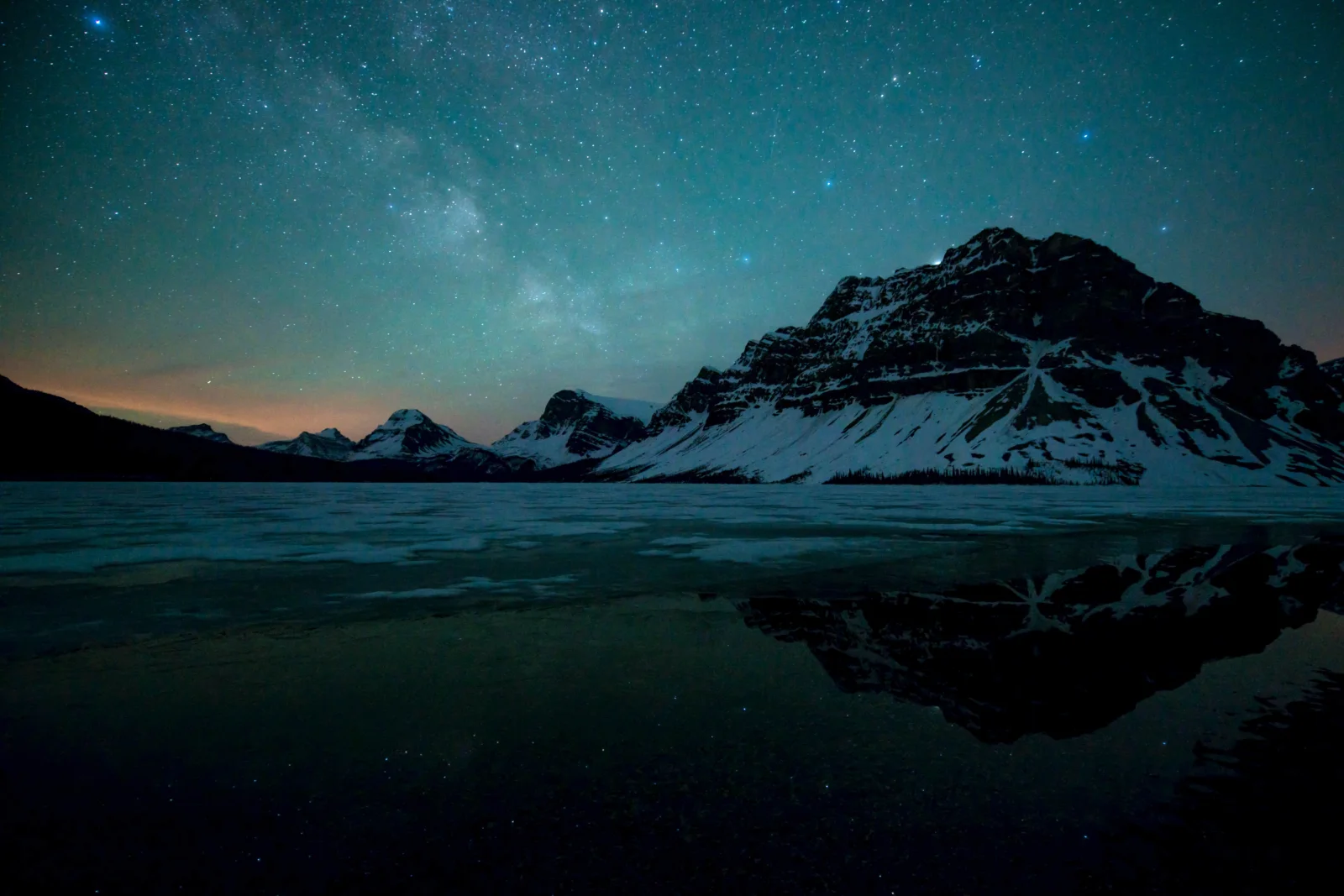 夜空中的银河映照着雪山与湖面，远处山峰清晰可见。