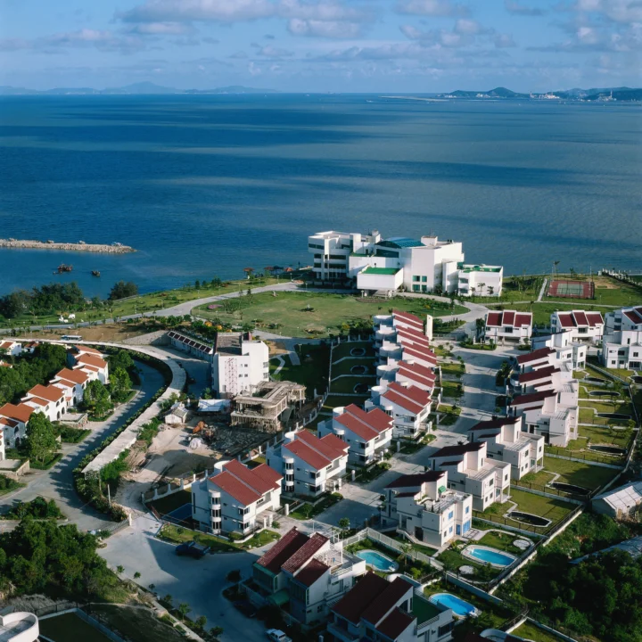 俯瞰海滨度假区、蓝色海湾、草地和成片的白色建筑。