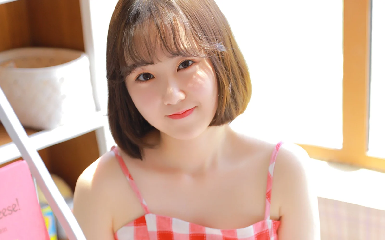 一位短发女性在明亮室内窗边面对镜头微笑。