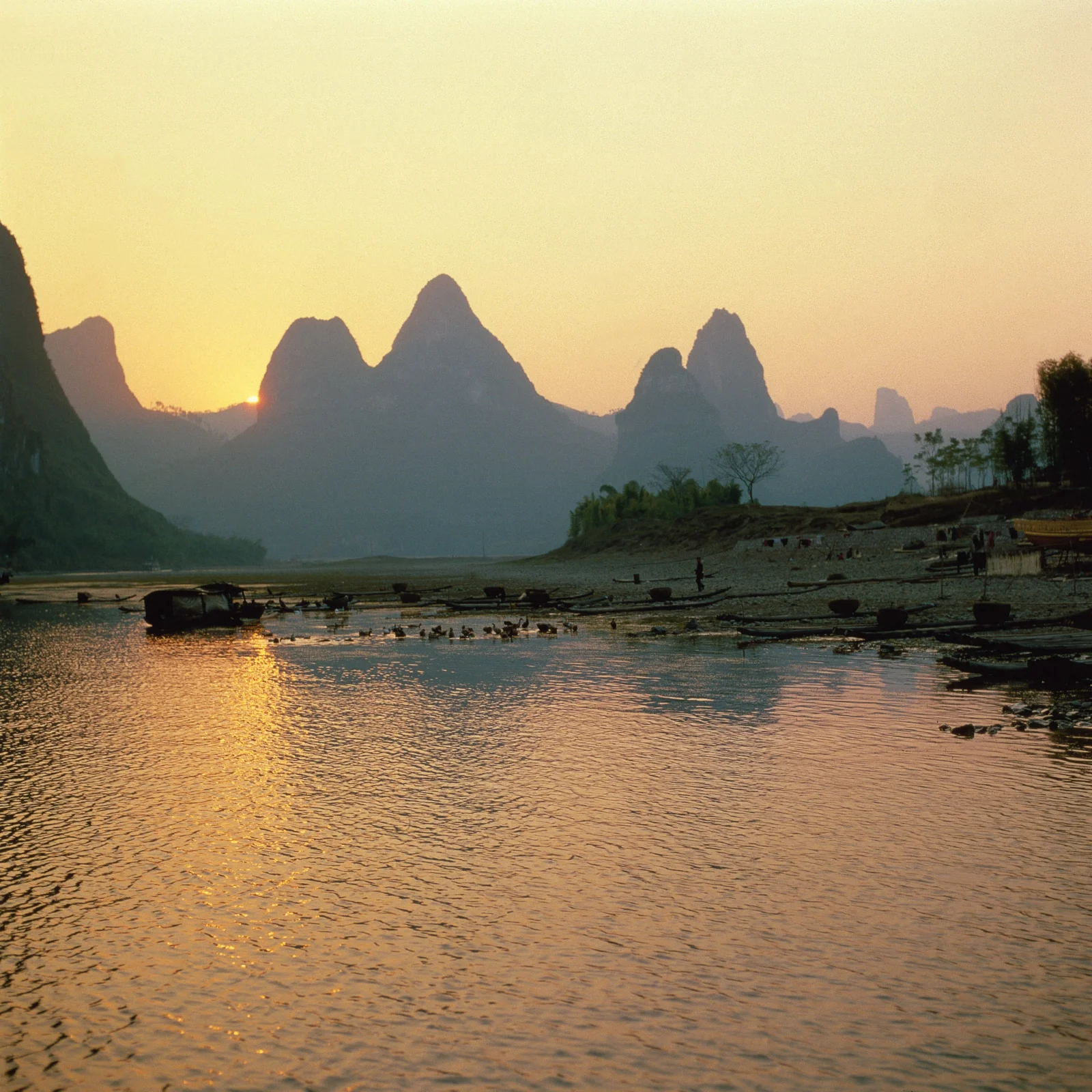 夕阳映照下，群山、江面与岸边小舟构成宁静的自然景色。
