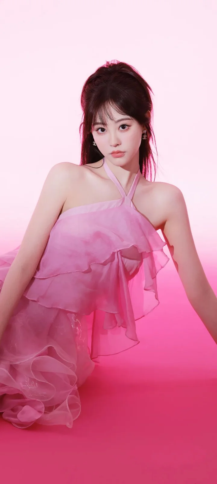 ピンクの重ねドレスを着た女性が、ピンクの背景の前でポーズを取っています。