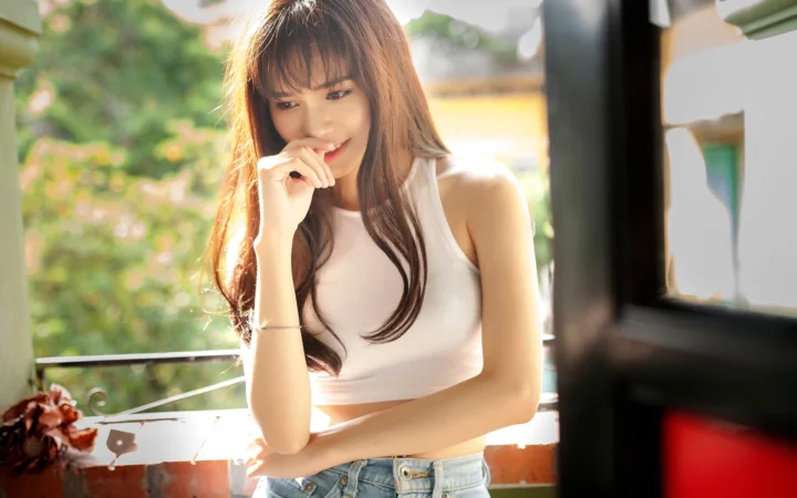 一名长发女子坐在明亮的窗边，阳光照亮了她的脸庞和白色上衣。