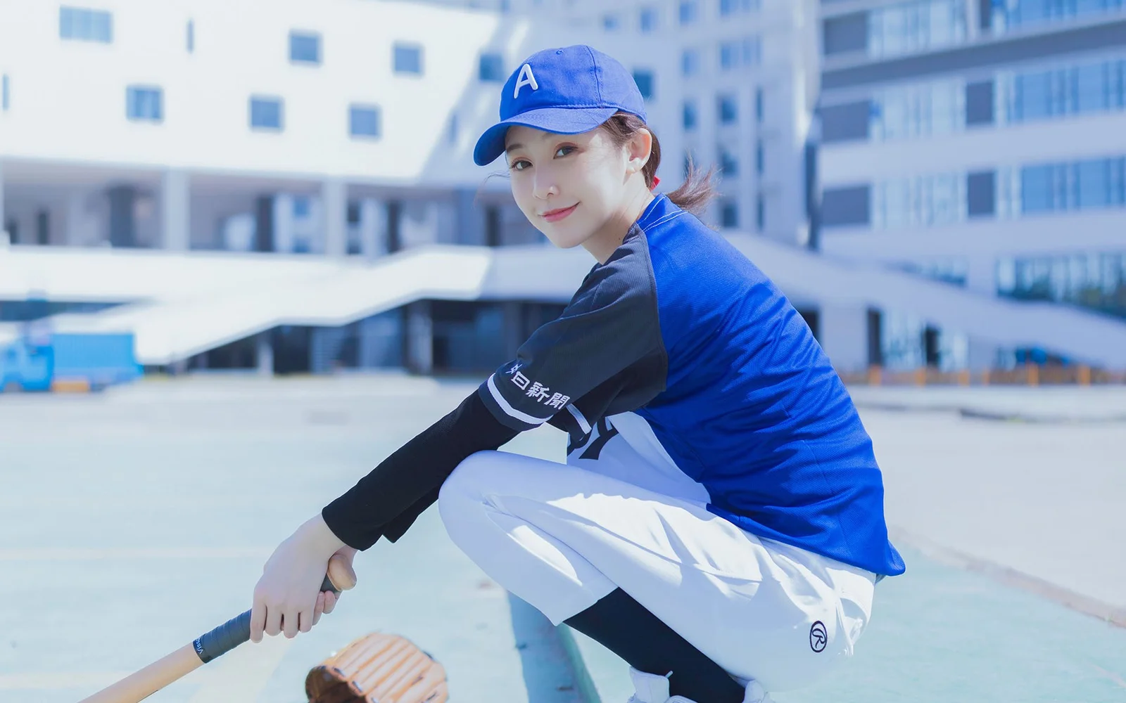 一名戴蓝色帽子的女性穿着运动服，在现代建筑旁户外蹲姿入镜。