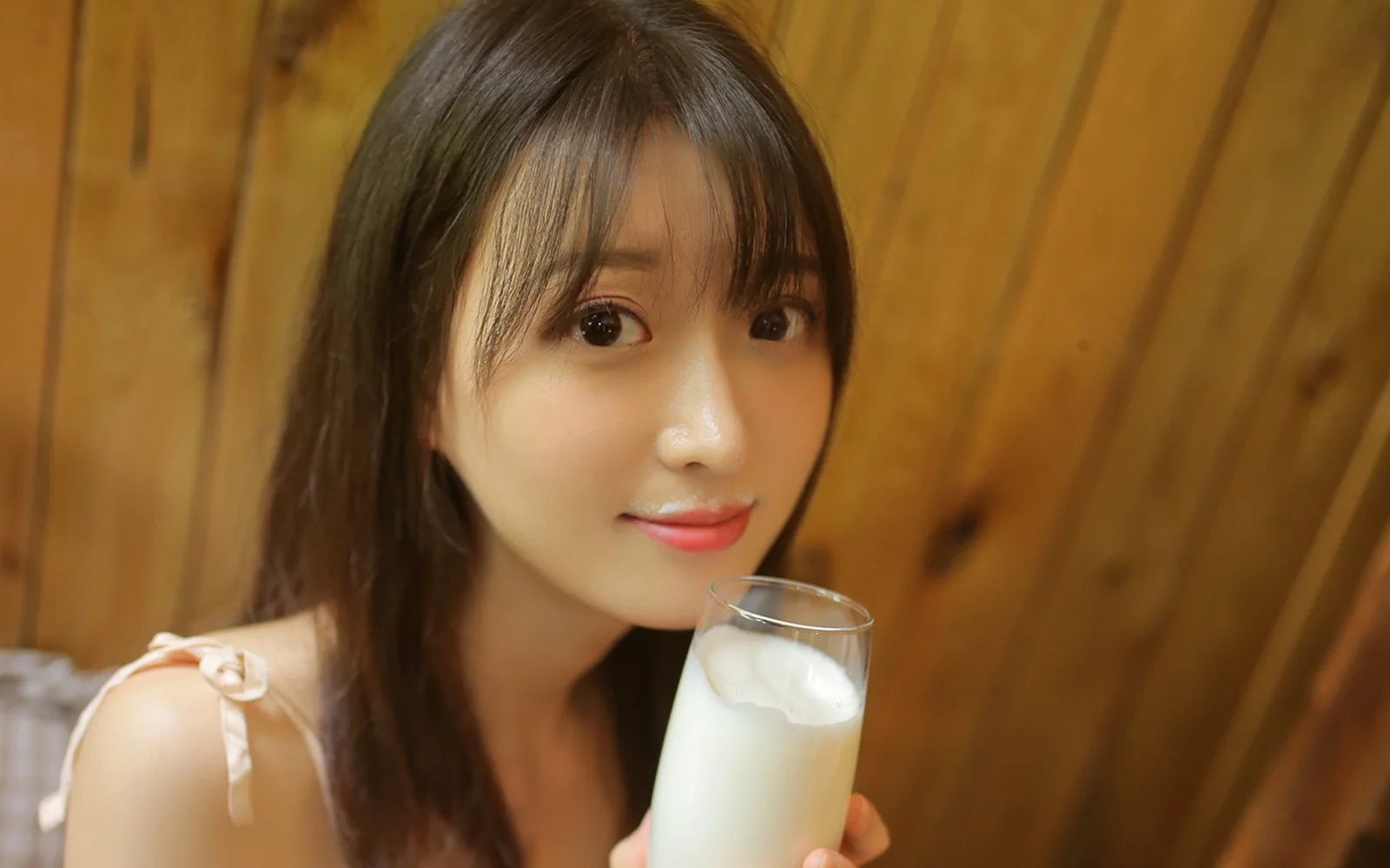 一位女性在木质墙壁前手持一杯牛奶。