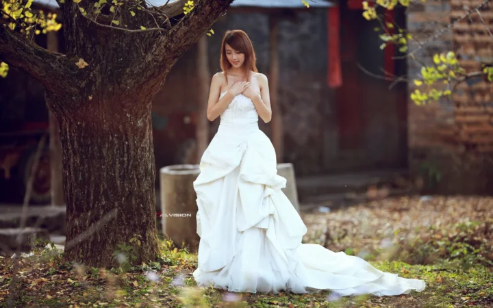 一名身穿白色婚纱的女性站在树下的庭院中。