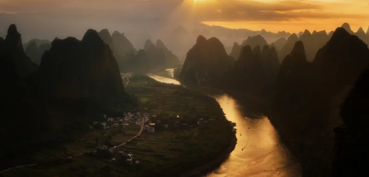 夕阳映照下，蜿蜒的河流穿过层叠的喀斯特山峰。