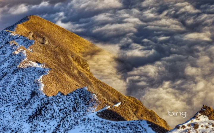 覆着积雪的山脊在金色光线下延伸，浓厚云层翻涌于山谷之间。