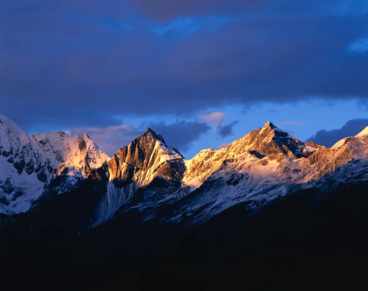 夕阳映照下的雪山群峰在深蓝色暮色天空下延展开来。