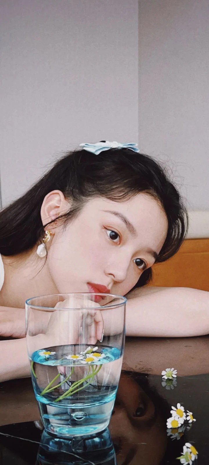一名女性靠在桌边，面前放着装有水和小花的玻璃杯。