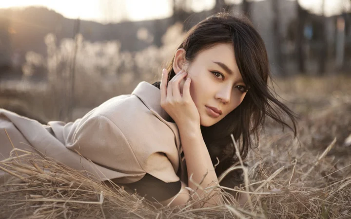 一名成年女性躺在秋日干草中，侧身看向镜头。