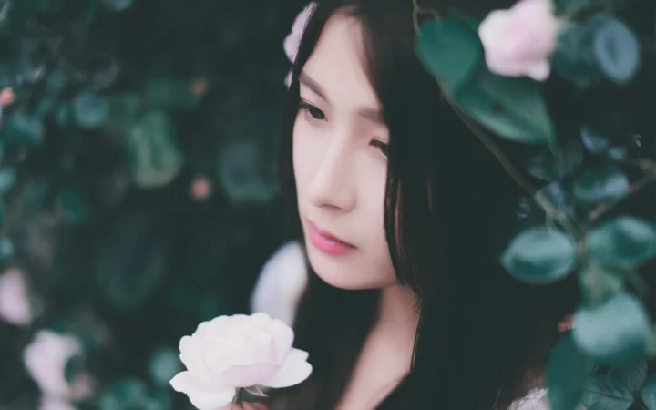 一位成年女性在绿叶与粉白花朵 વચ્ચે的侧脸肖像。