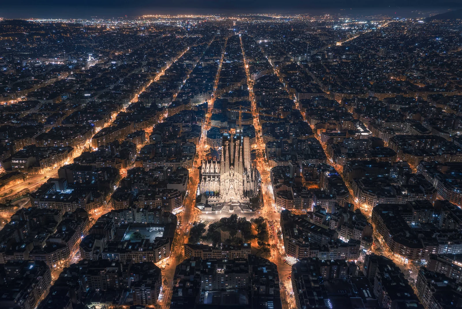 夜幕下的城市从高空俯瞰，中央一座灯火通明的尖顶建筑被纵横交错的街道环绕。