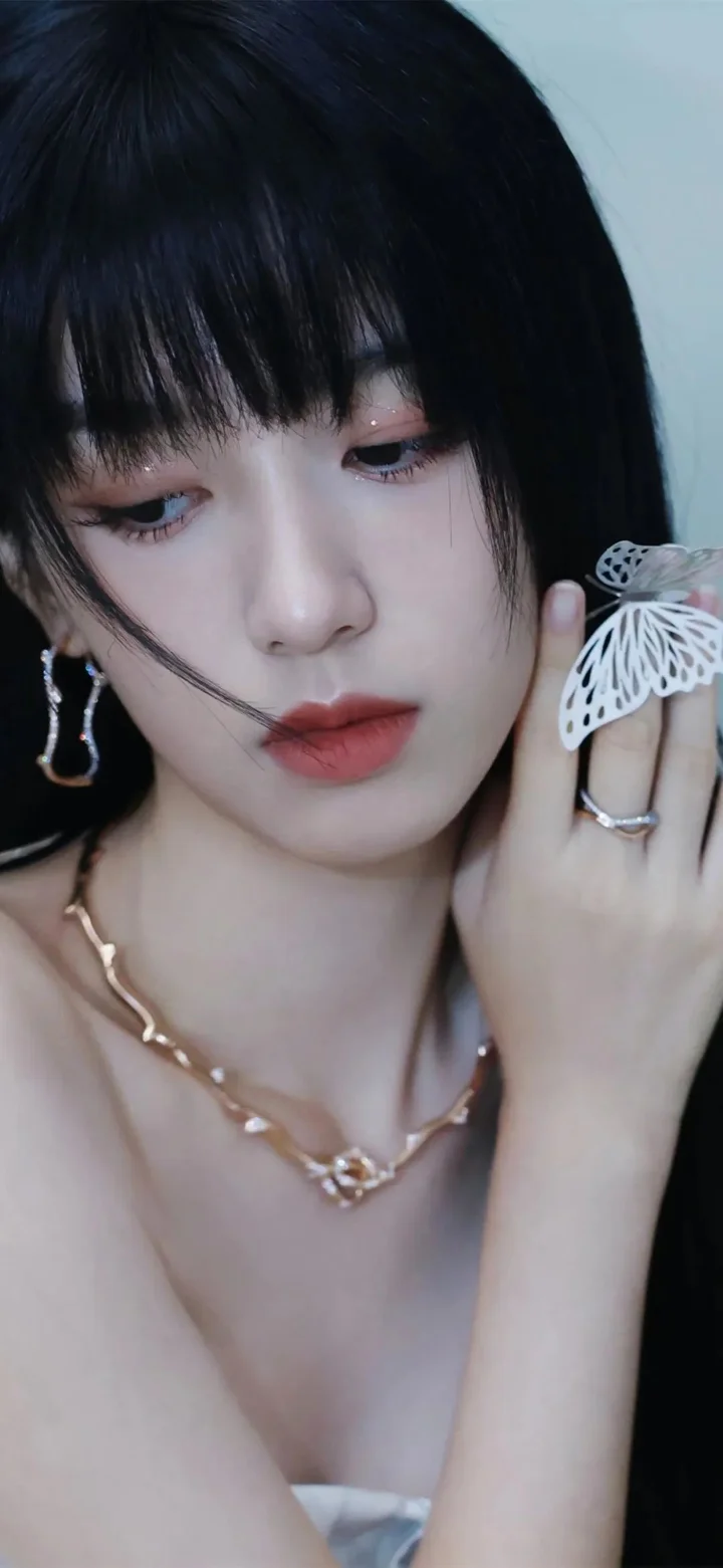 一位黑发女性近距离注视镜头，手持白色蝴蝶饰品，佩戴耳环和项链。