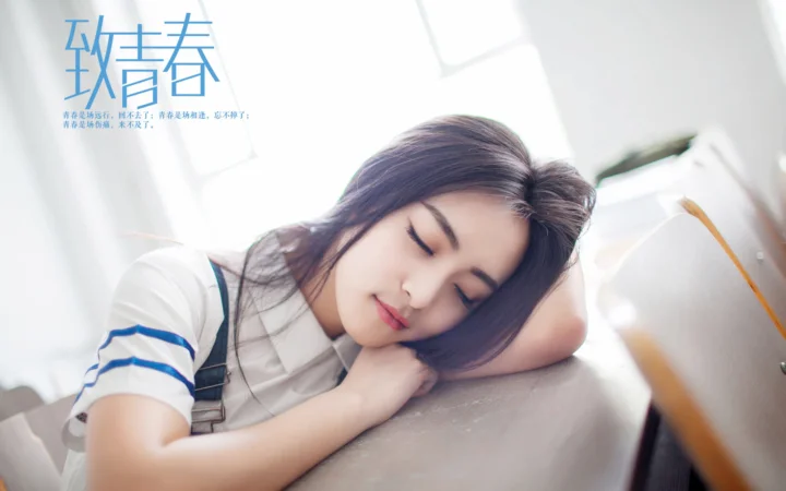 一名女子在明亮的窗边桌前闭眼小憩。