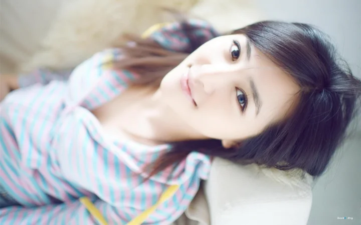 一位深色长发女性穿着浅色条纹上衣，面向镜头呈现柔和肖像。