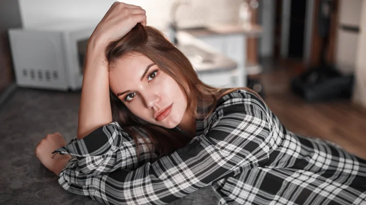 一名成年女性穿着黑白格纹衬衫，俯身躺在室内地毯上看向镜头。