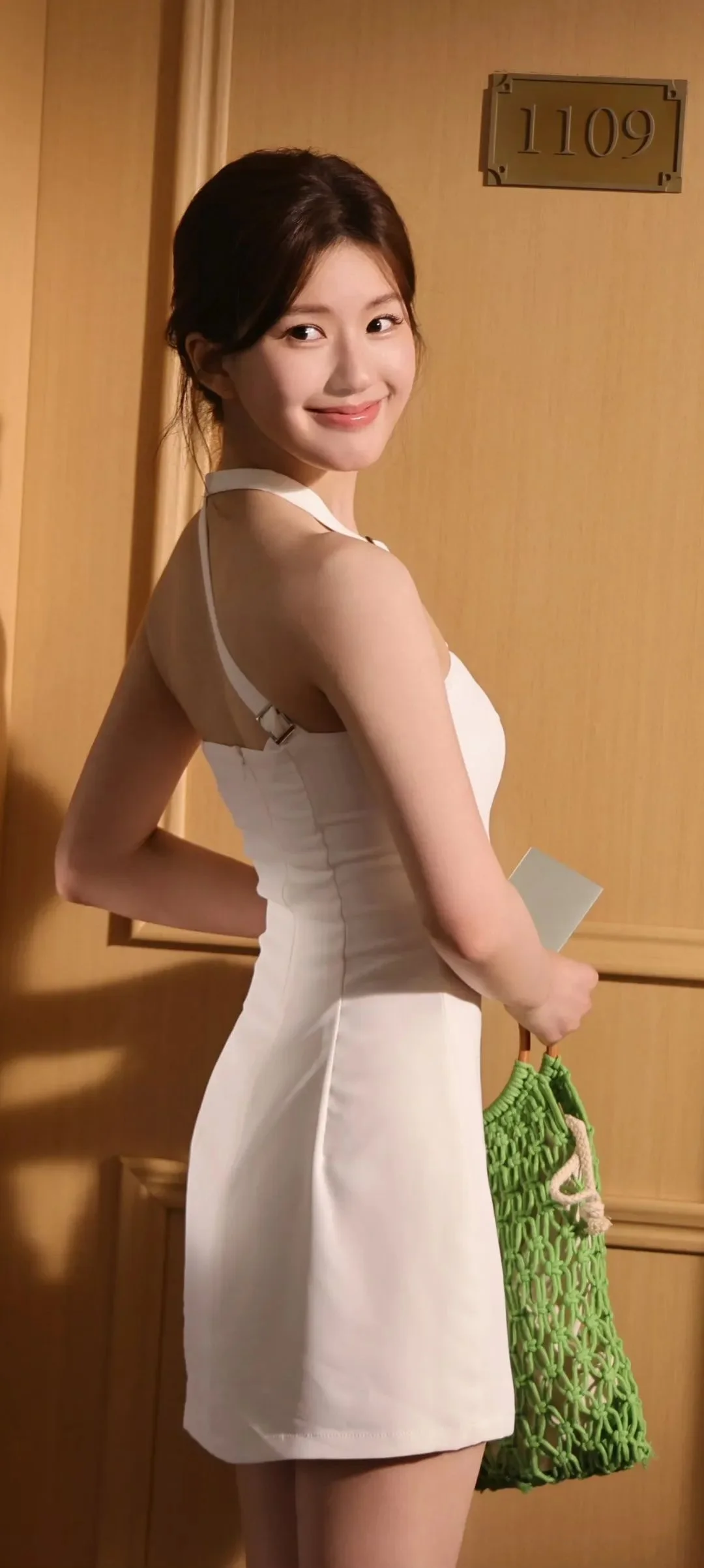 一名穿白色连衣裙的女子站在木门前，手提绿色网袋并回头看向镜头。