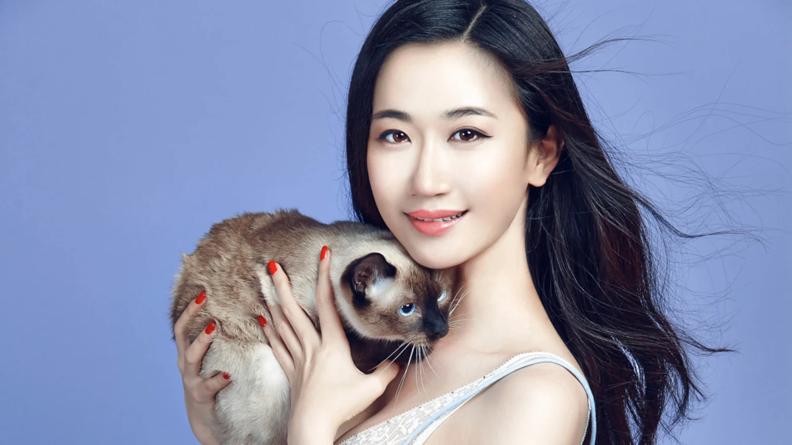 긴 머리의 여성이 파란 배경 앞에서 고양이를 안고 미소 짓고 있다.