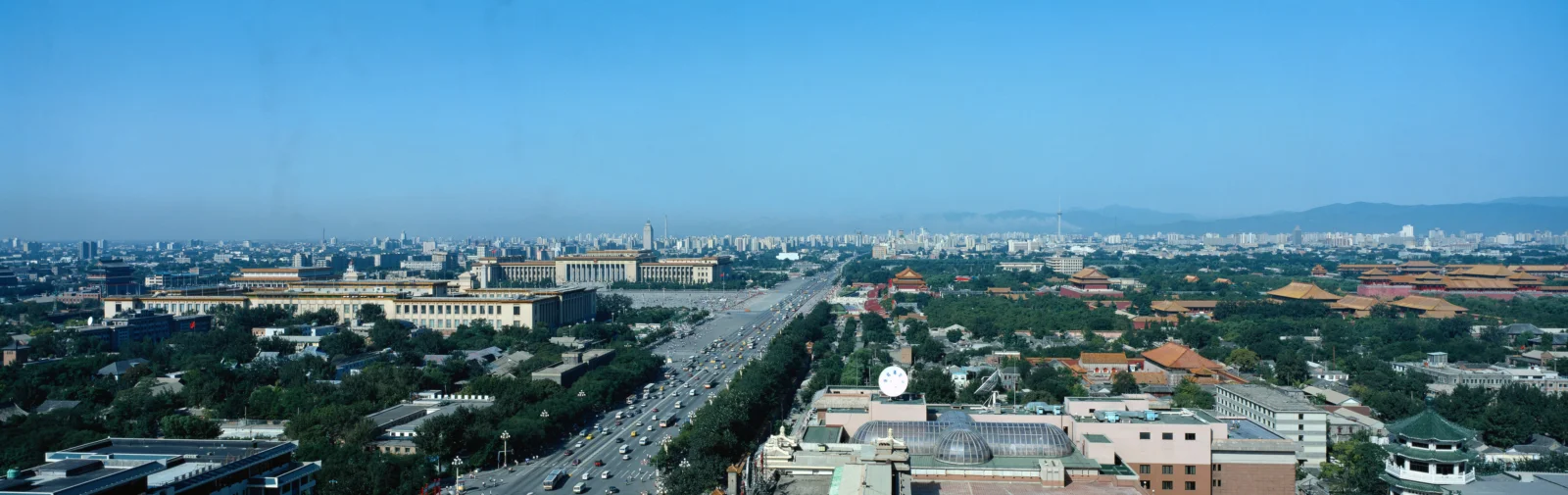 城市全景中，一条宽阔的城市道路穿过成片建筑与绿地，远处延伸至天际线。