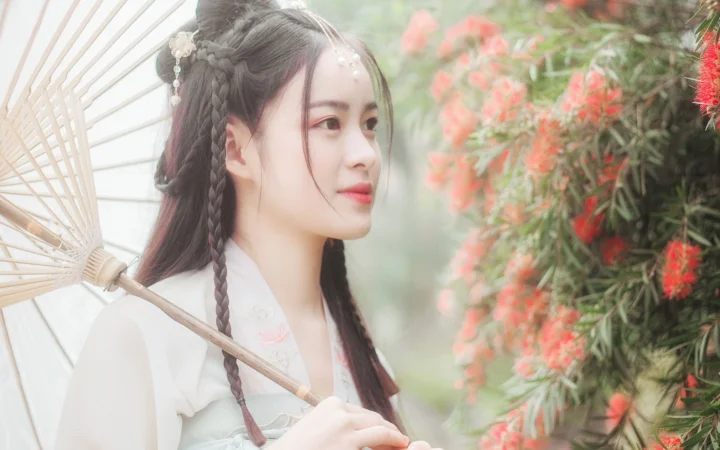一位身穿浅色传统服饰的女子手持纸伞站在花丛旁。