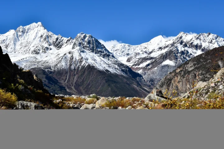 蓝天下连绵的雪山矗立在岩石遍布的山谷背景中。