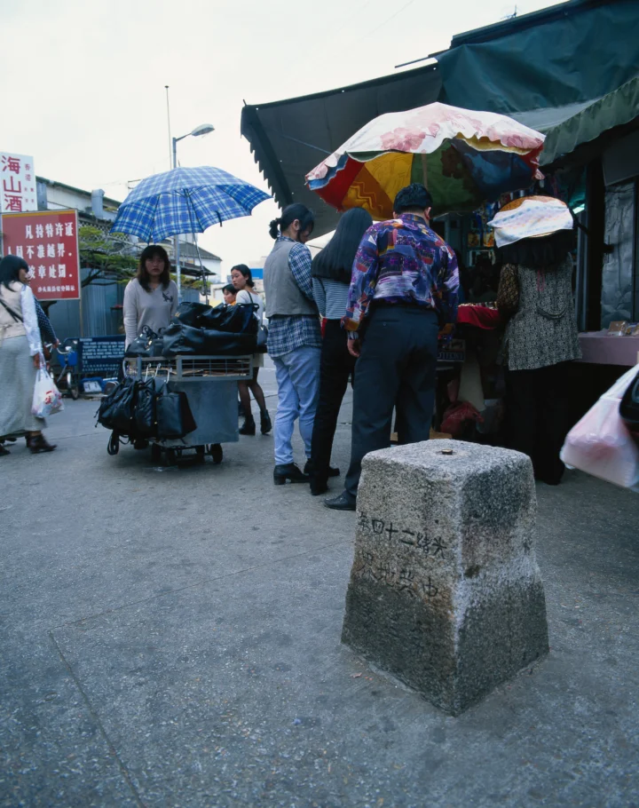 一条城市街道上的集市摊位、行人和雨伞构成了热闹的街景。