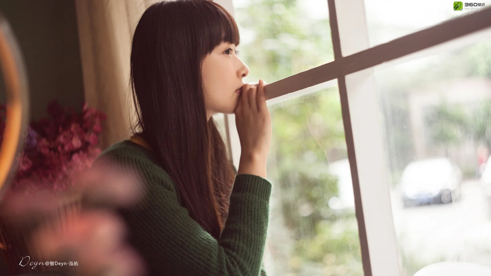 一名穿深色针织衫的女性站在窗边侧身望向窗外。