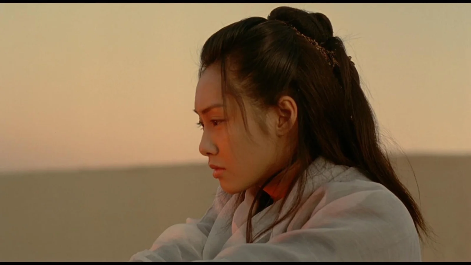 一名长发女性身穿浅色衣物，在温暖的夕阳背景前呈侧面轮廓。