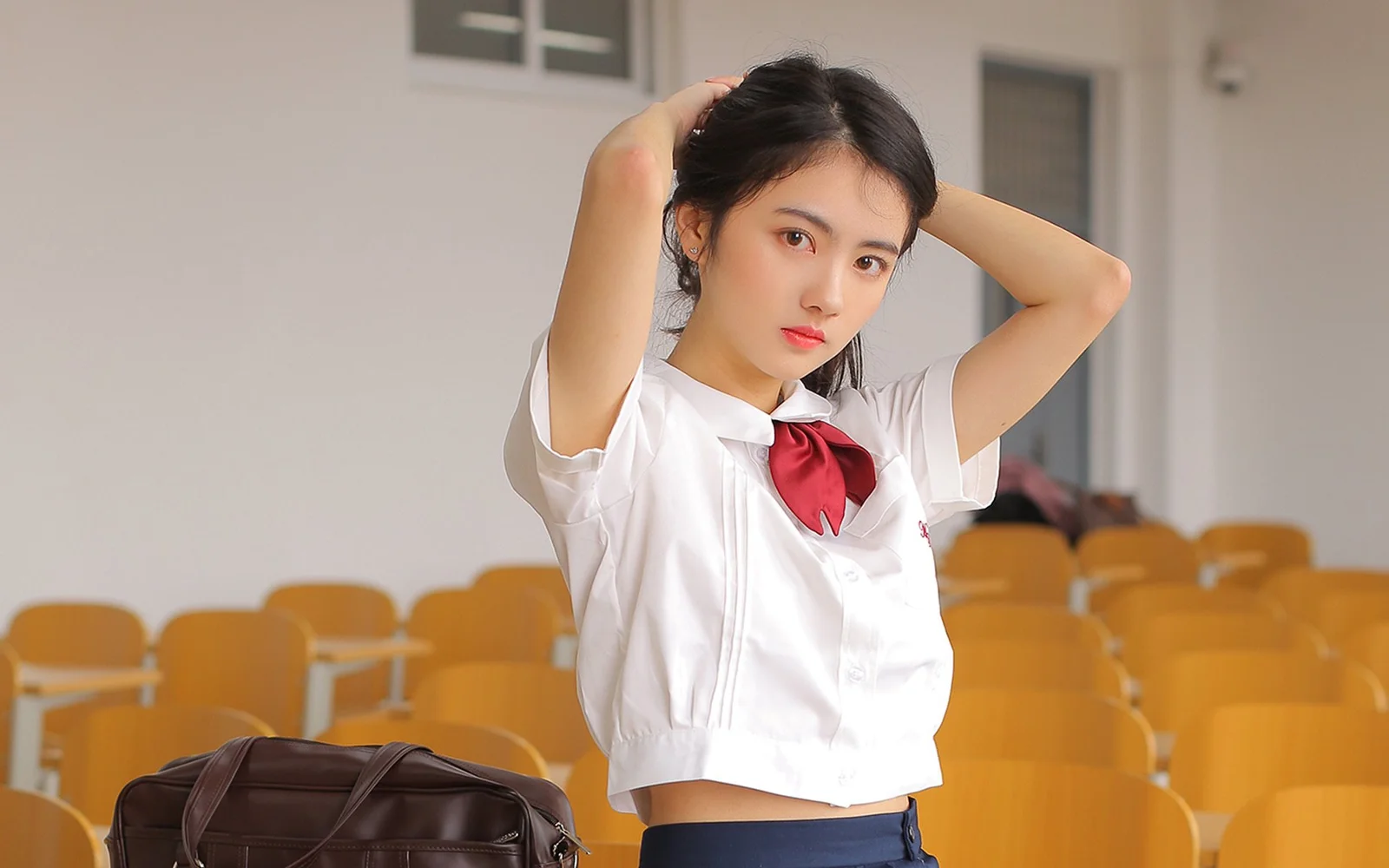 一名身穿白色上衣和红色领结的女性在教室座椅前整理头发。