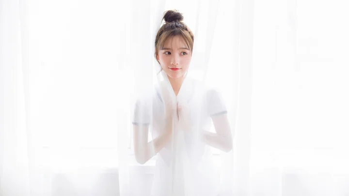 一名成年女子站在明亮的白色纱帘后。