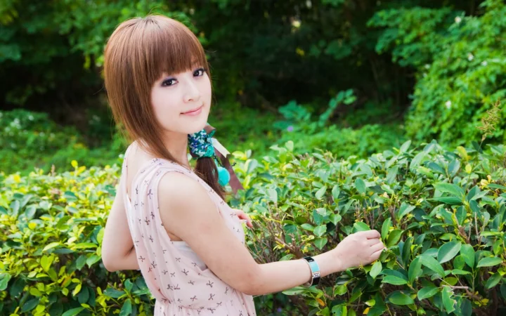一名女子站在户外的绿色植物间，回头面向镜头微笑。