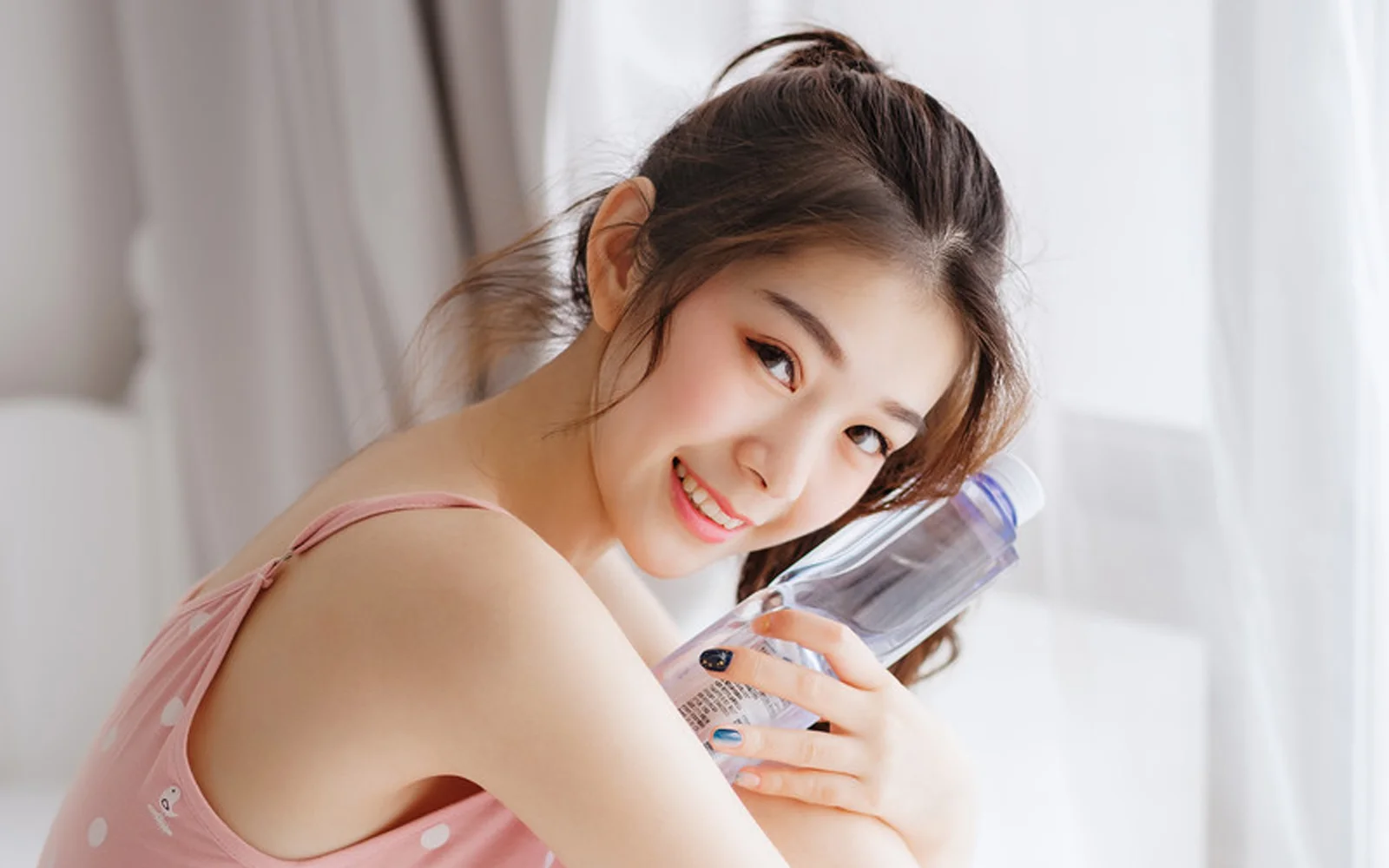 一位身穿粉色上衣的成年女性在室内微笑并手持透明瓶子。