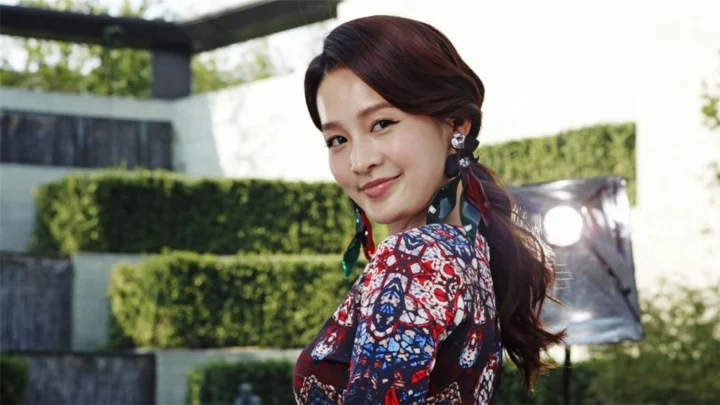 一位成年女性身穿彩色图案服装站在修剪整齐的绿篱前。