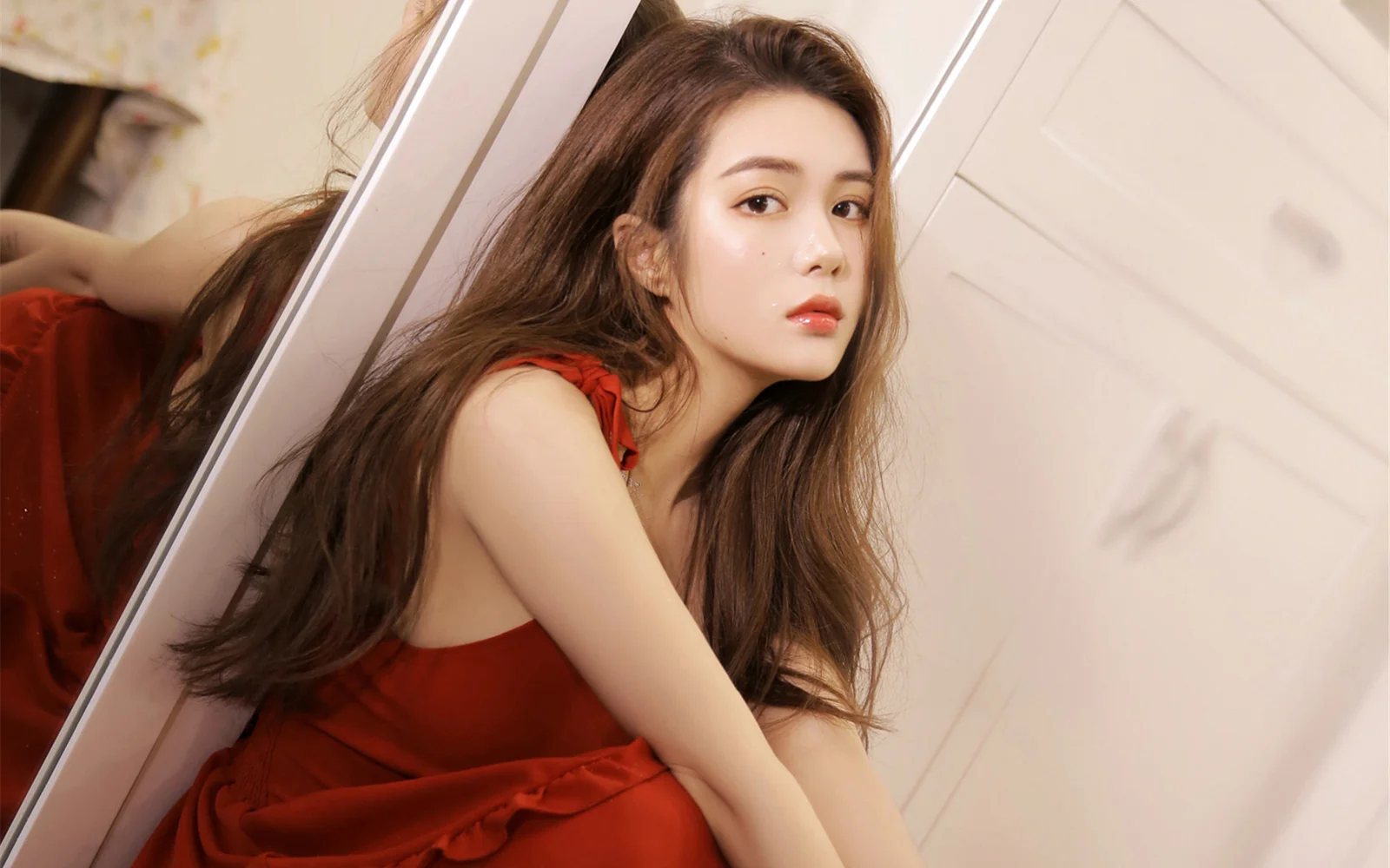 긴 머리의 여성이 빨간 드레스를 입고 거울 옆에 앉아 있습니다.