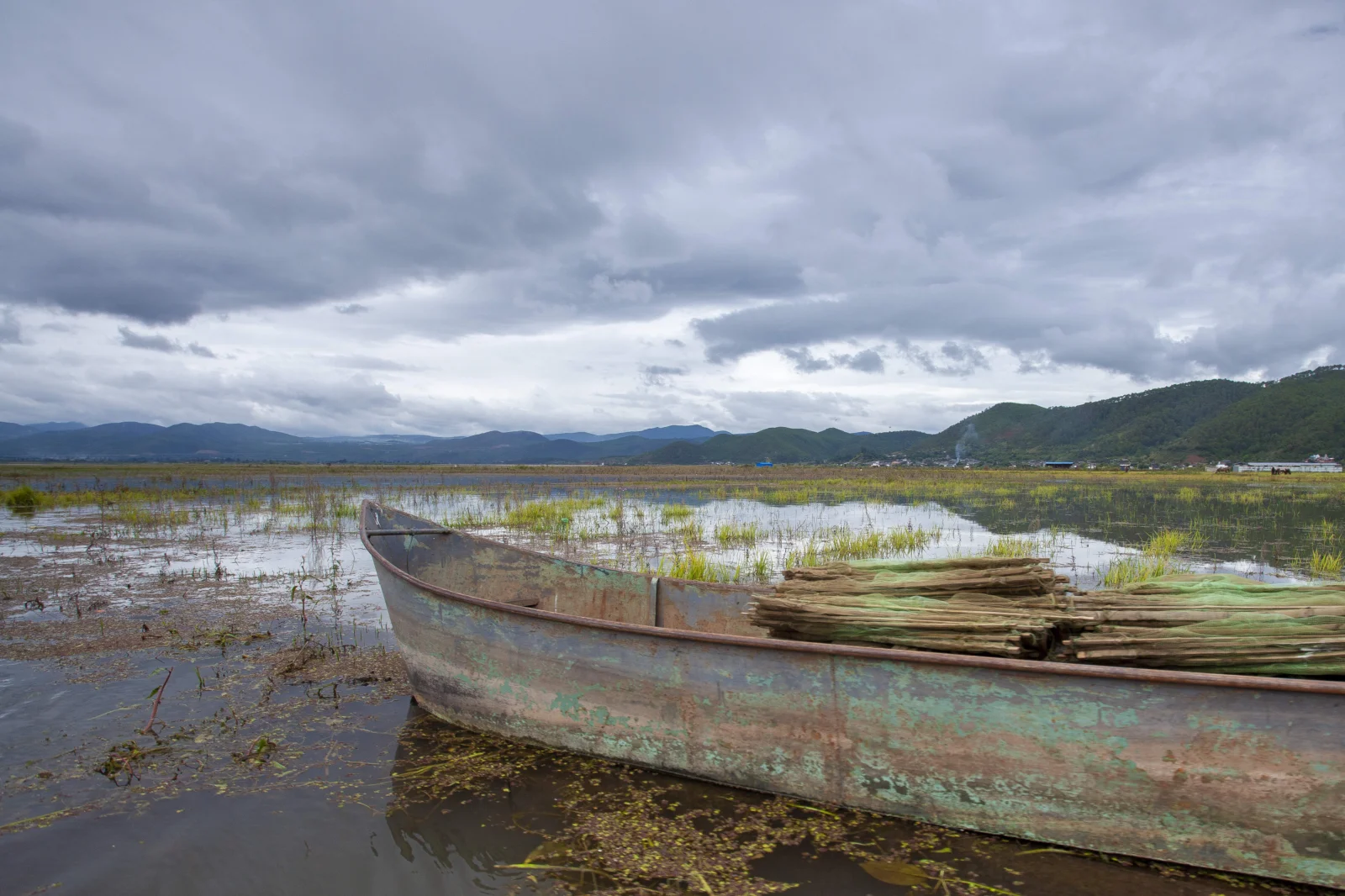 古びた木 boat が広い湿地に浮かび、遠くに山々と厚い雲が広がっています。