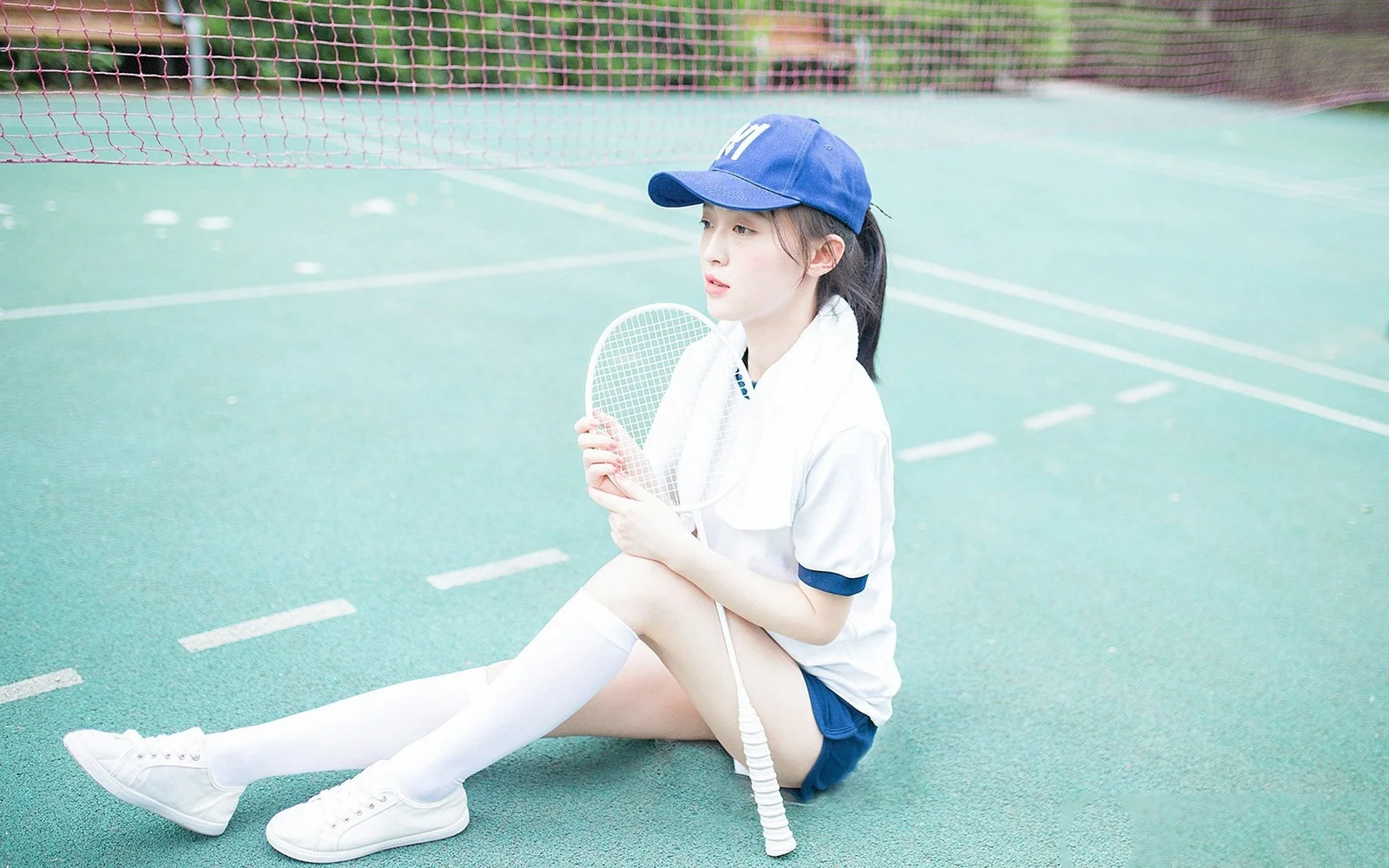 一名戴藍色帽子的女性坐在球場上，手持羽毛球拍。