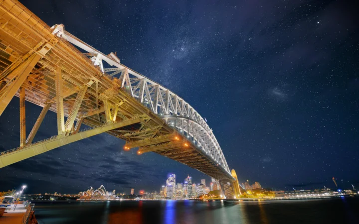 夜空下灯光璀璨的悬索桥横跨水面，远处是城市夜景。
