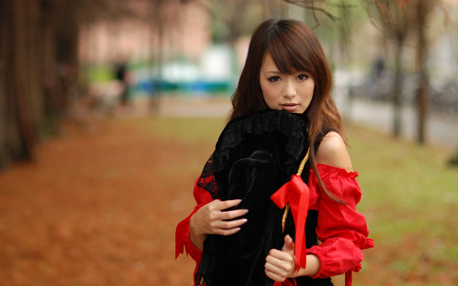 一名成年女子在户外穿着红色上衣，怀抱一个黑色物体。