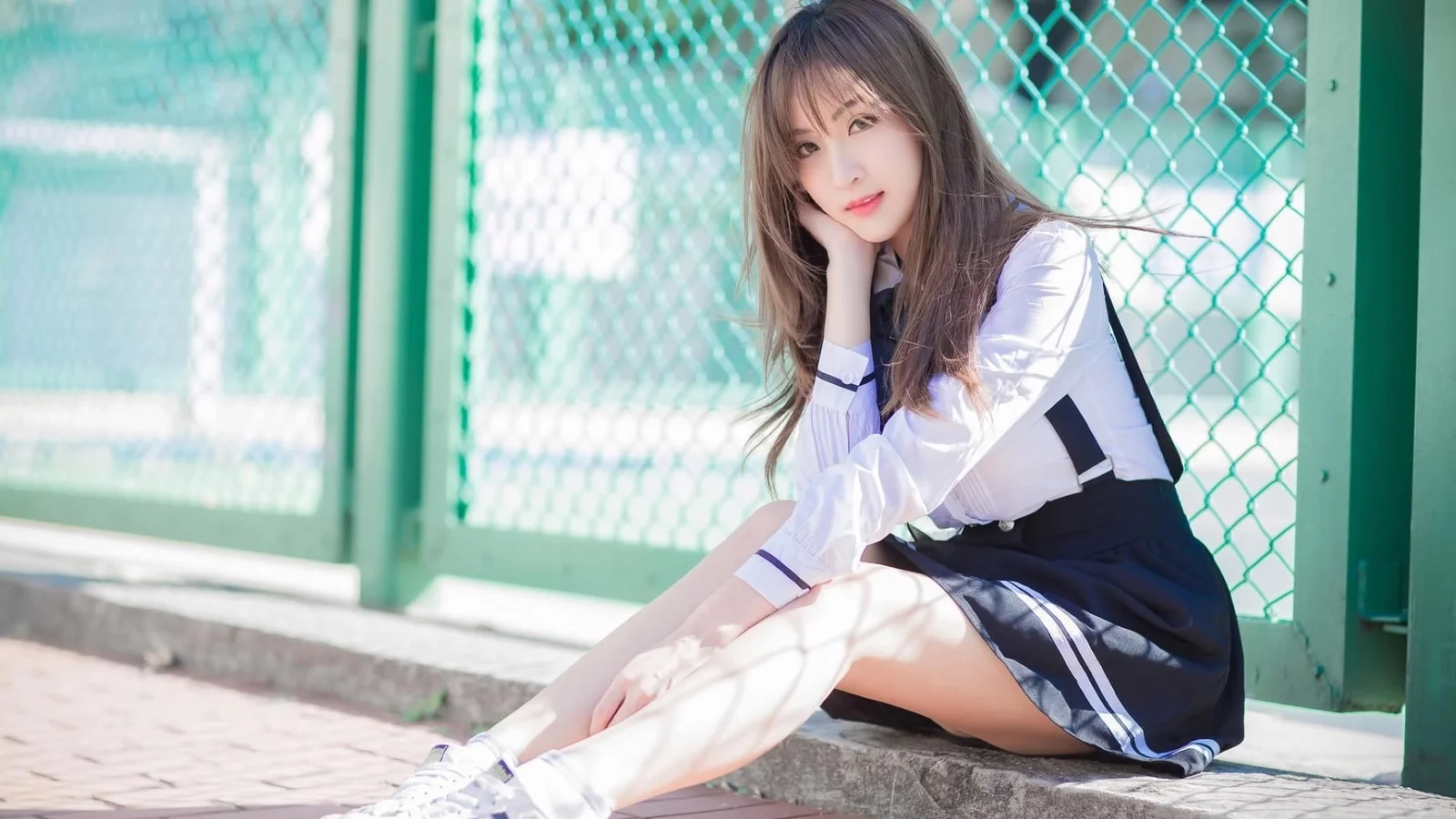 야외의 초록색 철망 울타리 옆 계단에 여성이 앉아 있습니다.