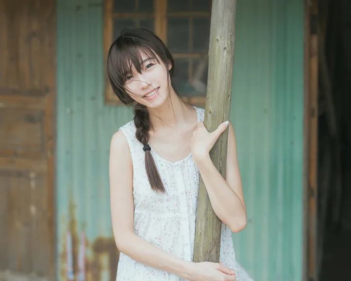 一名扎着辫子的女性在木屋旁微笑并倚靠着木柱。