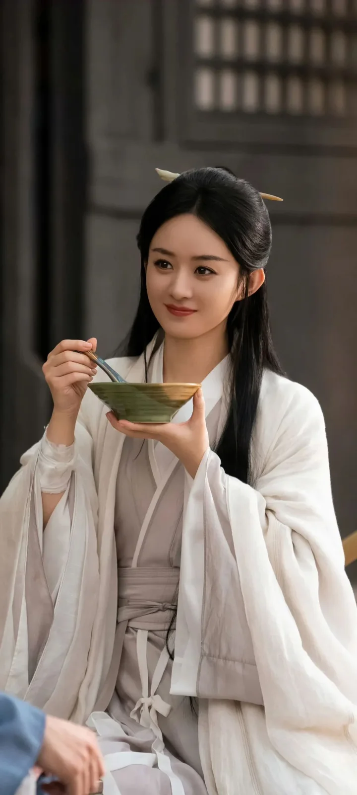 一名身穿白色传统服饰的女子在室内手持碗和勺子。