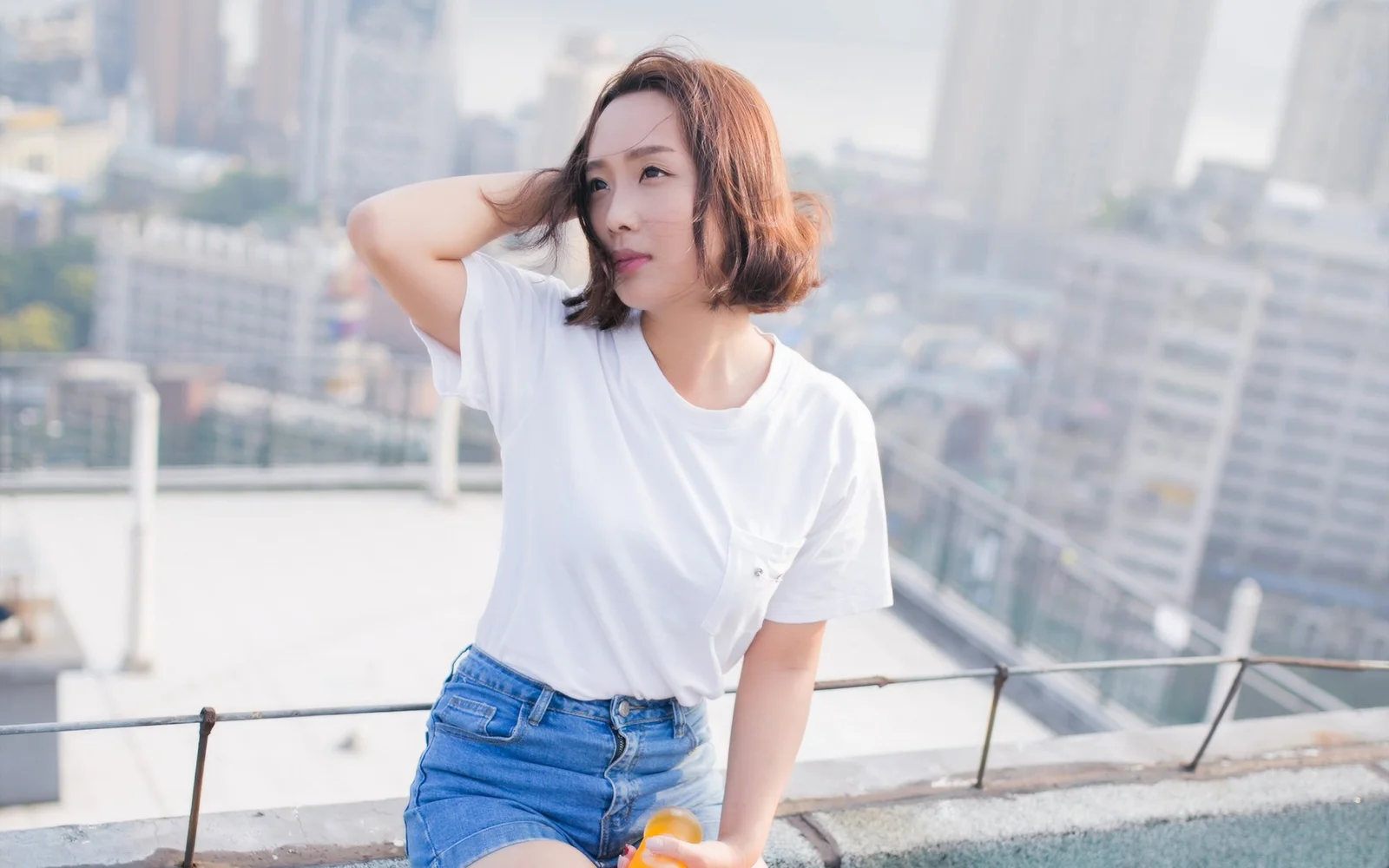 성인 여성이 옥상에 서 있으며 뒤로 밝은 도시 고층 건물이 보입니다.