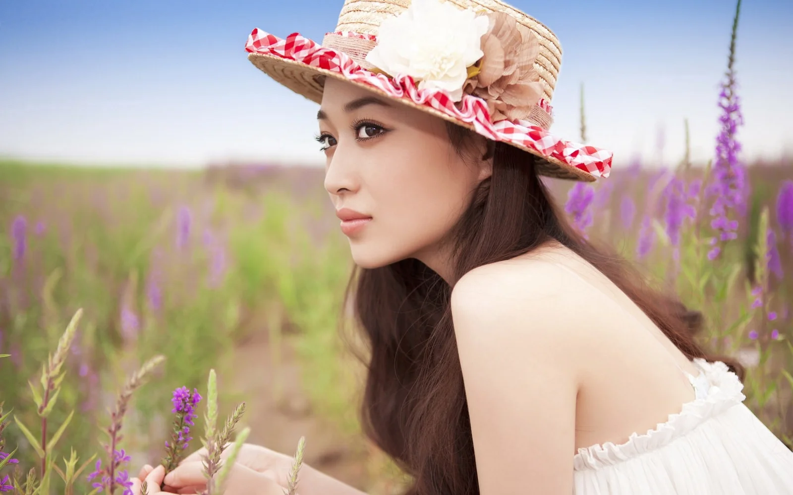 一名戴着装饰花朵草帽的女子坐在紫色花朵盛开的田野中。