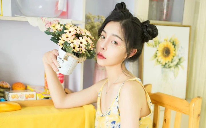 一位成年女性在室内手捧花束坐在桌旁。